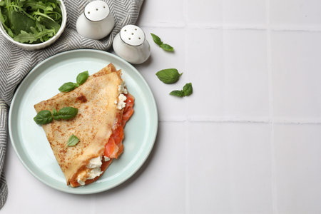 Delicious crepe with salmon, cream cheese, basil and arugula on white tiled table, flat lay. Space for textの写真素材