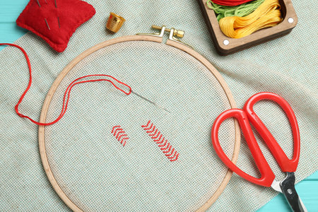 Embroidery. Canvas with cross stitches and supplies on turquoise wooden table, flat layの写真素材