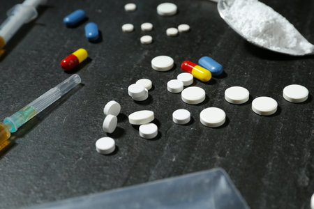 Drug addiction. Pills, syringes and spoon with powder on dark textured table, closeup