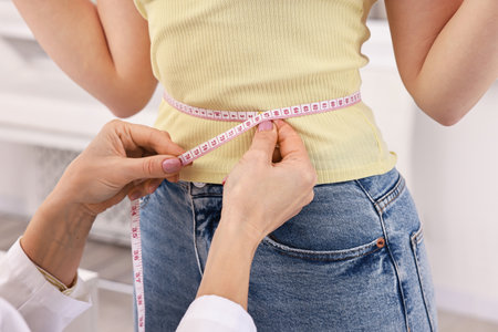 Weight loss. Nutritionist measuring patient's waist with tape in clinic, closeupの写真素材