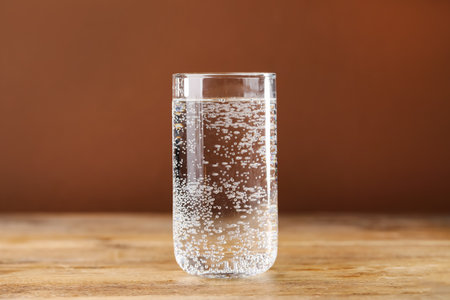Refreshing soda water with ice cubes in glass on wooden table against brown background, closeupの写真素材