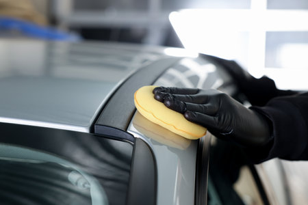 Man polishing car with yellow sponge indoors, closeupの写真素材