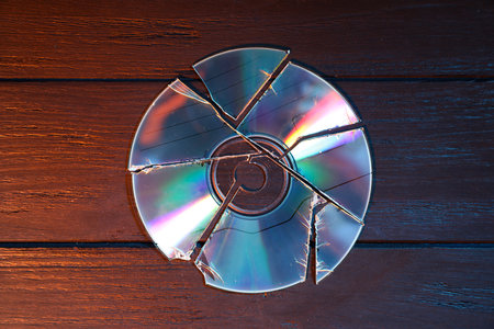 Broken compact disc on wooden background, top viewの写真素材