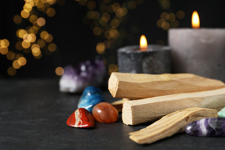 Palo santo sticks, gemstones and burning candles on black table against blurred lights, closeup. Space for textの写真素材
