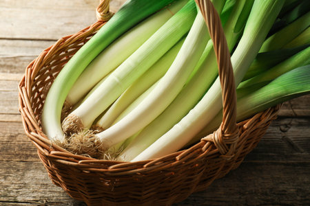 Fresh leeks in wicker basket on wooden table, closeupの写真素材