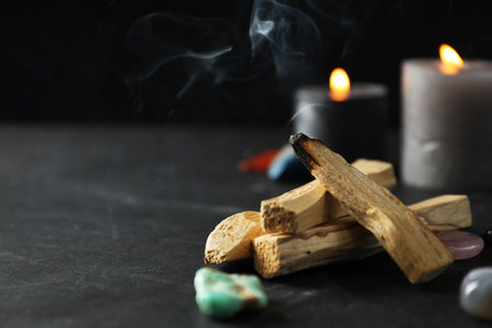 Smoldering palo santo stick, gemstones and burning candles on black table, closeup. Space for textの写真素材