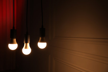 Glowing light bulbs hanging indoors, space for textの写真素材
