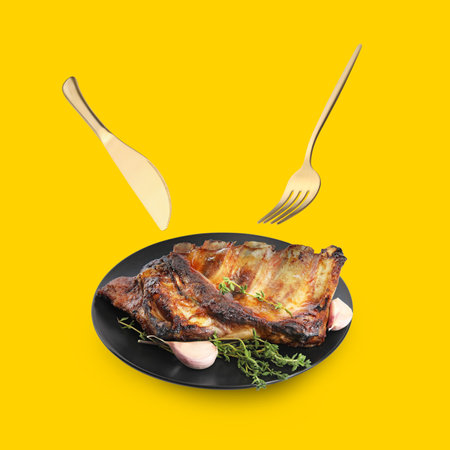 Cutlery in air over plate with tasty grilled ribs on golden backgroundの写真素材