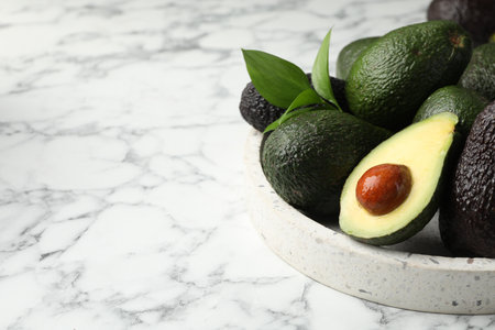 Whole and cut avocados on white marble table, closeup. Space for textの写真素材