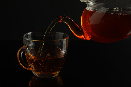 Pouring freshly brewed tea from teapot into glass cup on black table, closeupの写真素材
