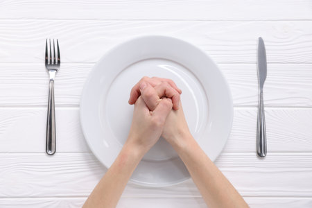 Woman holding hands together over plate and cutlery at white wooden table, top viewの写真素材