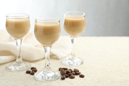 Coffee cream liqueur in glasses and beans on white textured table, space for text