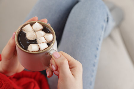 Woman holding mug of tasty hot chocolate with marshmallows on sofa, closeupの写真素材