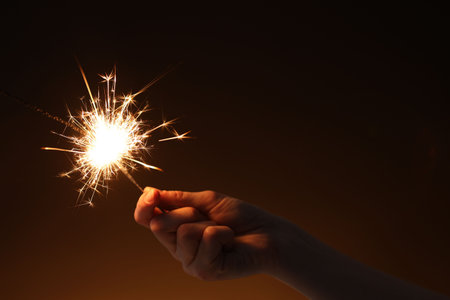 Woman with bright burning sparkler on dark background, closeupの写真素材