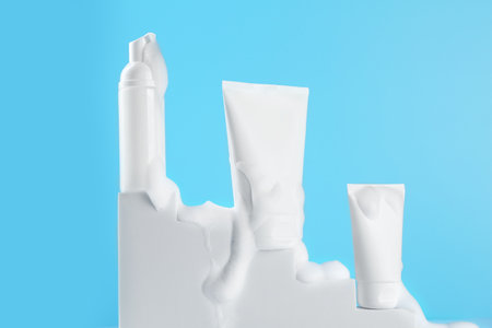 Tubes and bottle of cosmetic products with foam on podium against light blue backgroundの写真素材