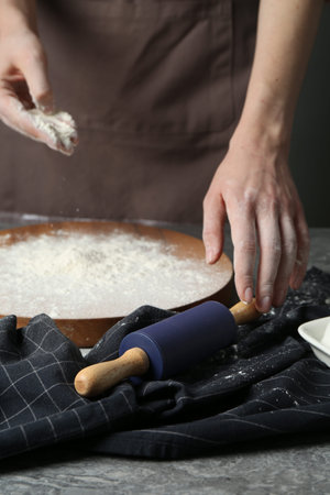 Woman with rolling pin and flour at gray table, closeup