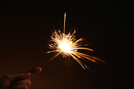 Woman with bright burning sparkler on dark background, closeupの写真素材