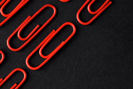 Red paper clips on black background, flat lay. Space for textの写真素材