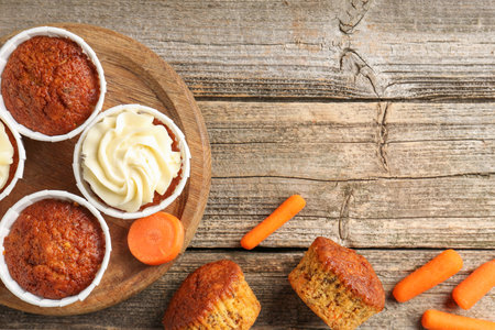 Delicious carrot muffins and fresh vegetables on wooden table, flat lay. Space for textの写真素材