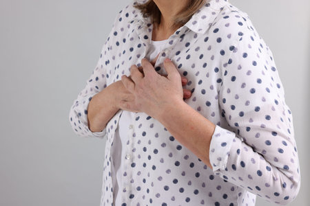 Heart attack. Senior woman suffering from pain in chest on light gray background, closeup