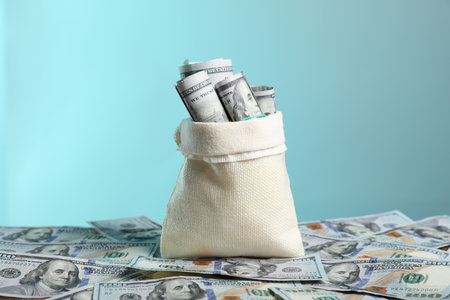 Burlap sack with dollar banknotes against light blue backgroundの写真素材