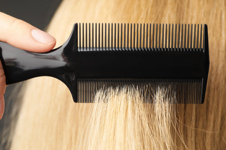 Woman brushing hair with plastic comb on grey background, closeup