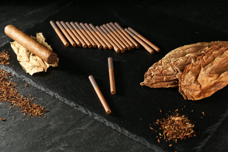 Tobacco, dried leaves, cigarettes and cigar on black table