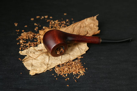 Tobacco, dried leaves and smoking pipe on black wooden table, closeup