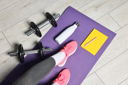 Woman with gym equipment and planner on floor indoors, above view