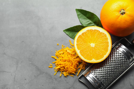 Pile of fresh orange zest, fruits, leaves and grater on grey textured table, flat lay. Space for textの写真素材