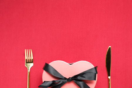 Heart shaped romantic gift and cutlery on red background, top view. Space for textの写真素材