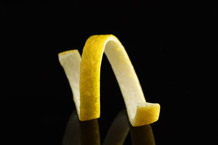 One curly lemon peel on black mirror surface, closeupの写真素材