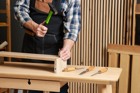 Senior man repairing wooden shelf with hammer and nail in workshop, closeup