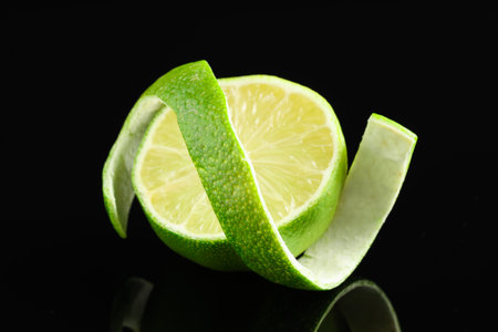 Fresh lime peel and half of fruit on black glass surface, closeupの写真素材
