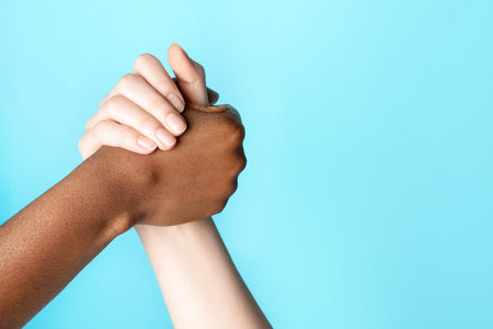 Stop racism. People of different skin colors holding hands on light blue background, closeup. Space for textの写真素材