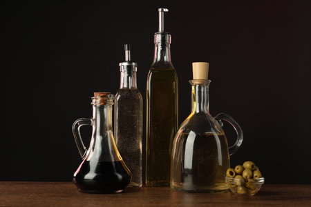 Salad dressings and olives on wooden table against dark backgroundの写真素材