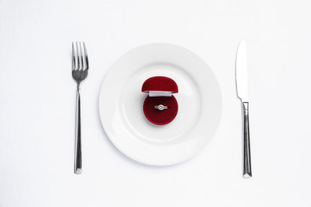 Beautiful engagement ring and setting for romantic dinner on white background, top viewの写真素材