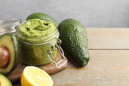 Tasty avocado dip in glass jar and fruits on wooden table, closeup. Space for textの写真素材