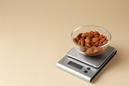 Electronic kitchen scale with almonds on beige background. Space for text