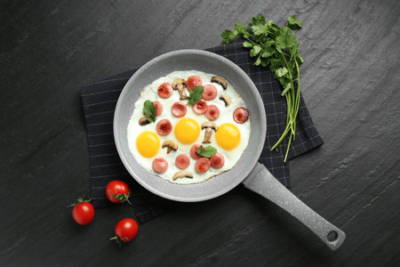Tasty fried eggs with cut sausages and mushrooms served on black table, flat layの写真素材