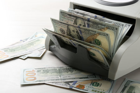 Money counter machine with dollar banknotes on white wooden table, closeupの写真素材