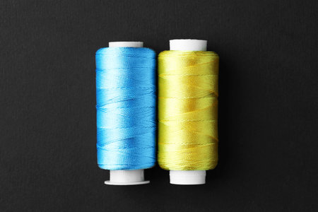 Spools of colorful sewing threads on black background, top view