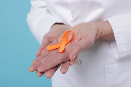 Multiple Sclerosis awareness. Doctor with orange ribbon on light blue background, closeup