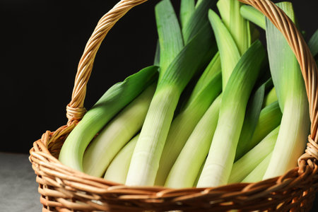 Fresh leeks in wicker basket on grey table, closeup