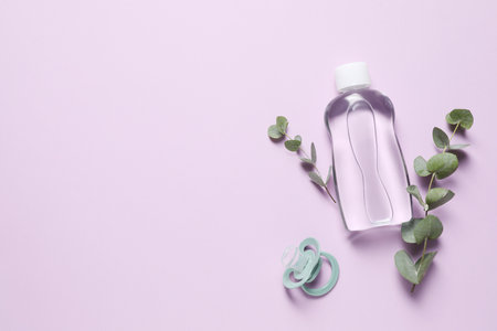 Baby oil, pacifier and eucalyptus on lilac background, top view. Space for textの写真素材