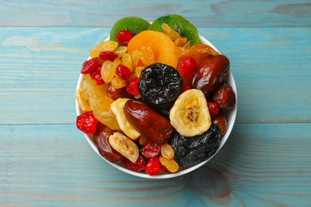 Mix of different dried fruits in bowl on blue wooden table, top view