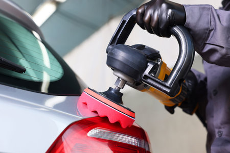 Man polishing car rear light with orbital polisher indoors, closeup