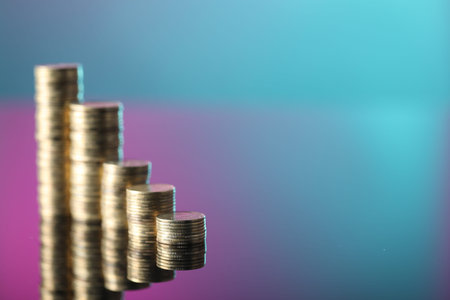 Stacks of coins on color mirror surface, closeup. Space for text