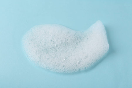 Sample of fluffy foam on light blue background, closeup