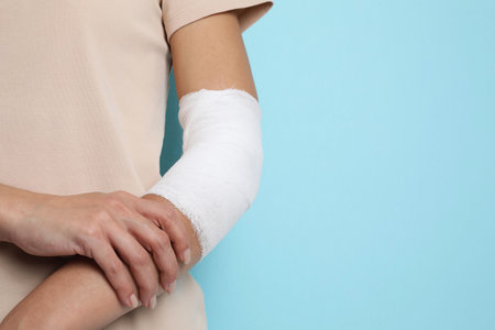 Woman with medical bandage on elbow against light blue background, closeup. Space for textの写真素材